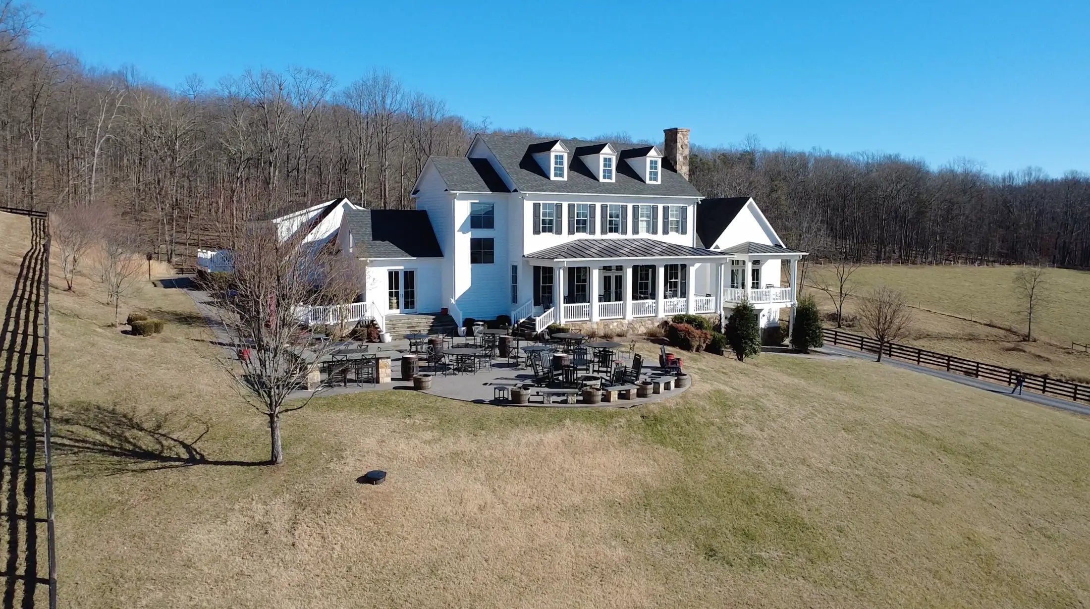 Large white house with black roof in a rural setting with trees and open fields.
