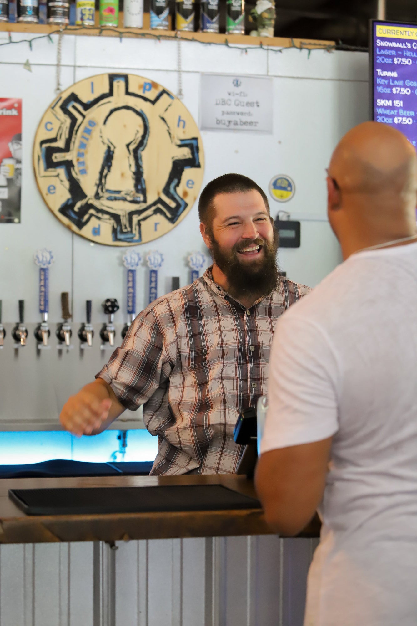 Man at a bar with a beer tap behind him and a sign on the wall.