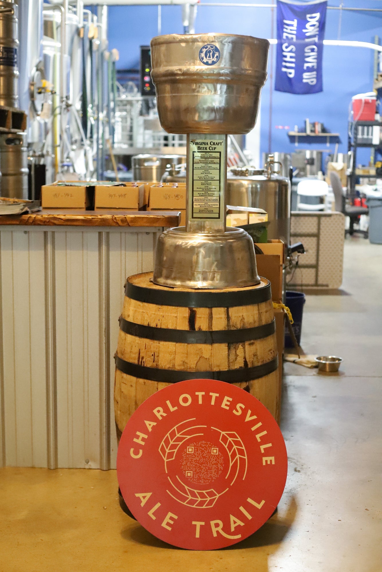 Virginia Craft Beer Cup on a wooden barrel with 'Charlottesville Ale Trail' sign in a brewery setting
