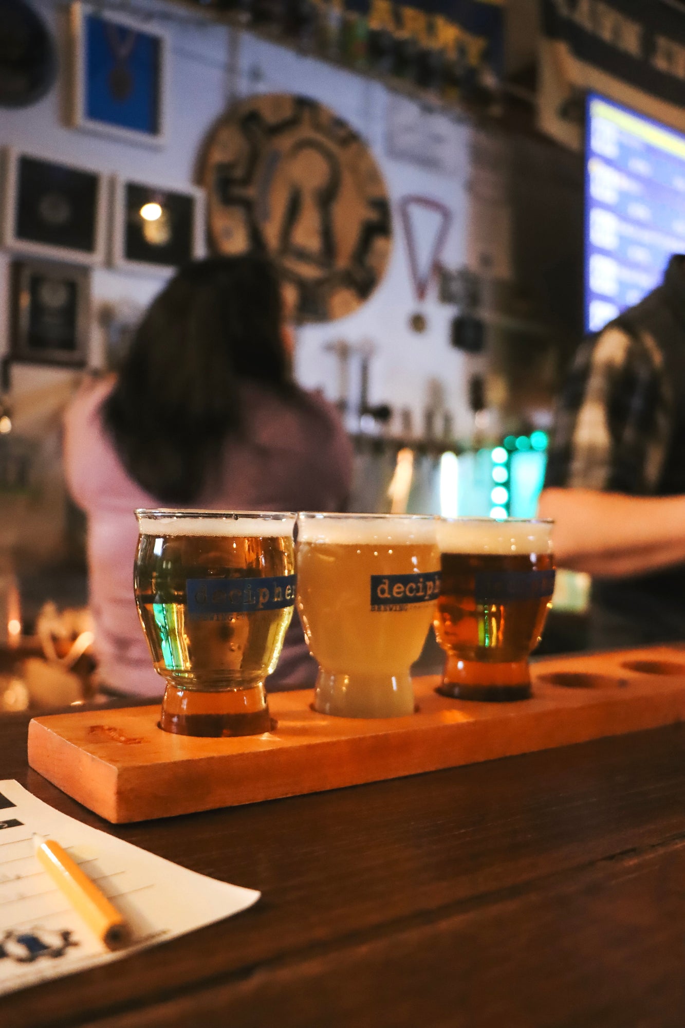 Three beer glasses on a wooden board with a blurred bar background