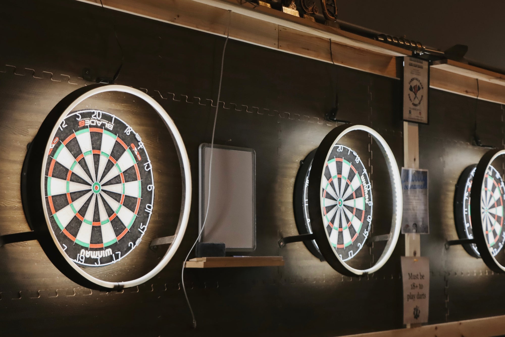Three illuminated dartboards mounted on a wall.
