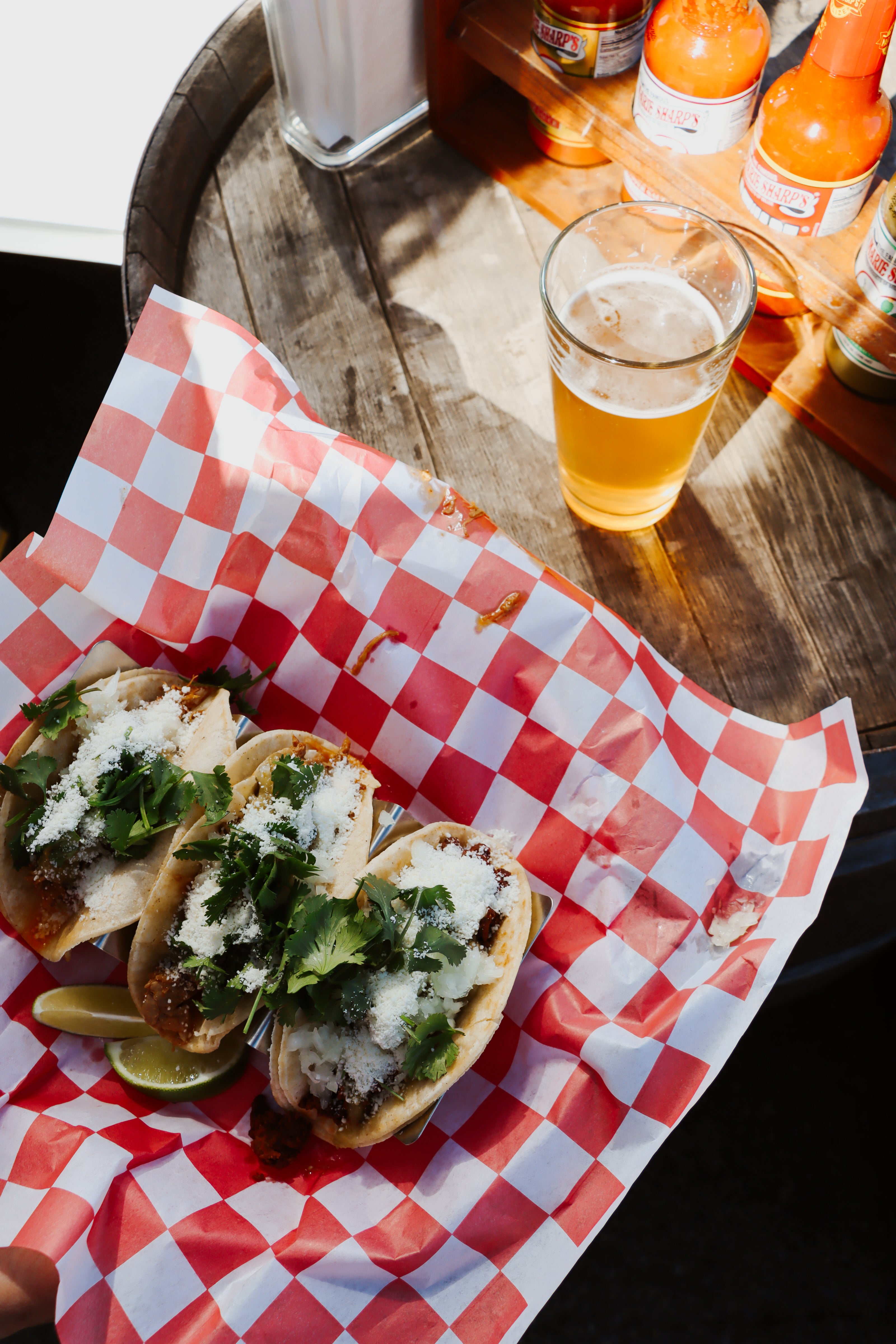 Tacos on a checkered paper with a glass of beer on a wooden table