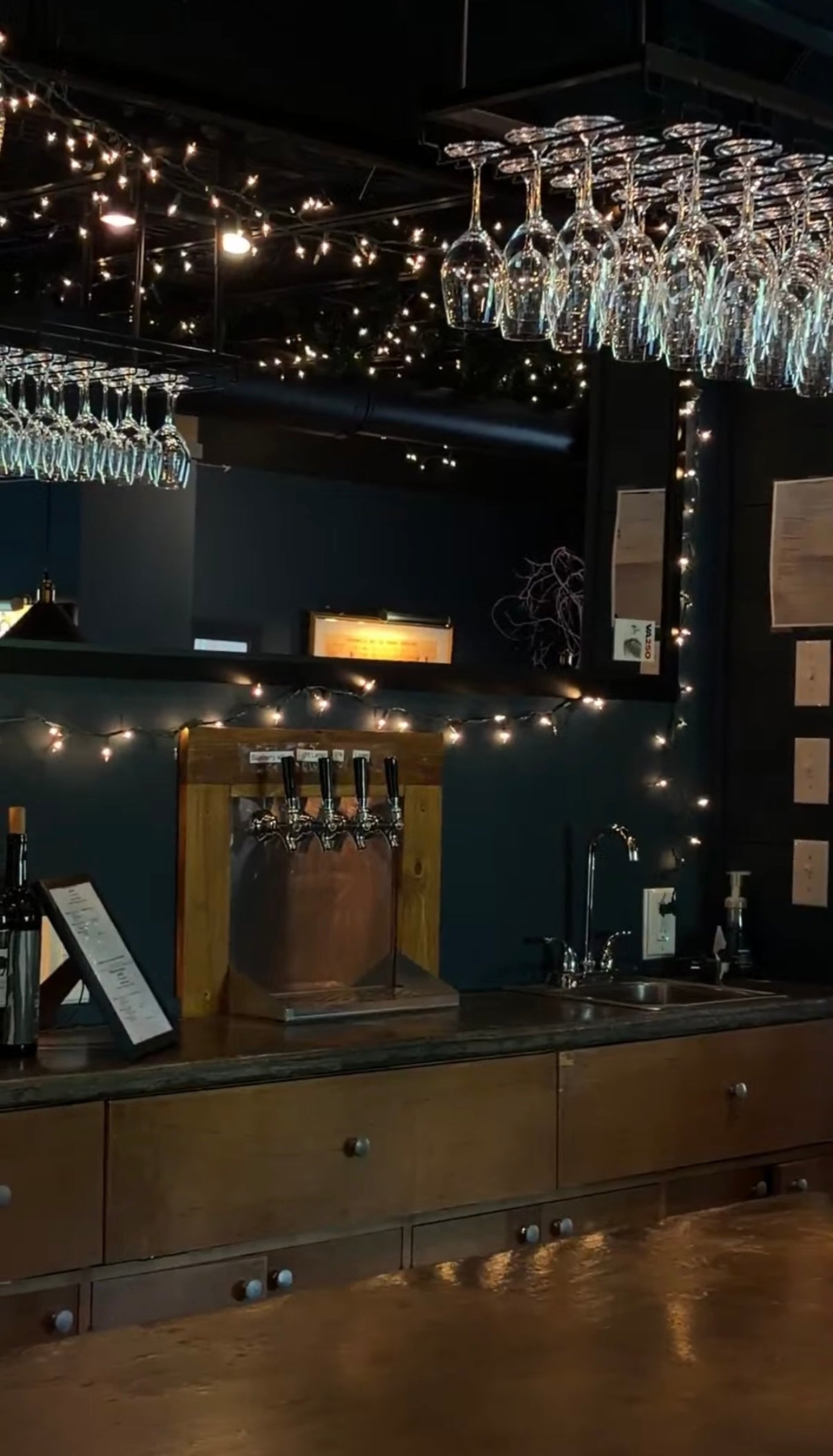 Bar counter with wine glasses, lights, and a dark wall.