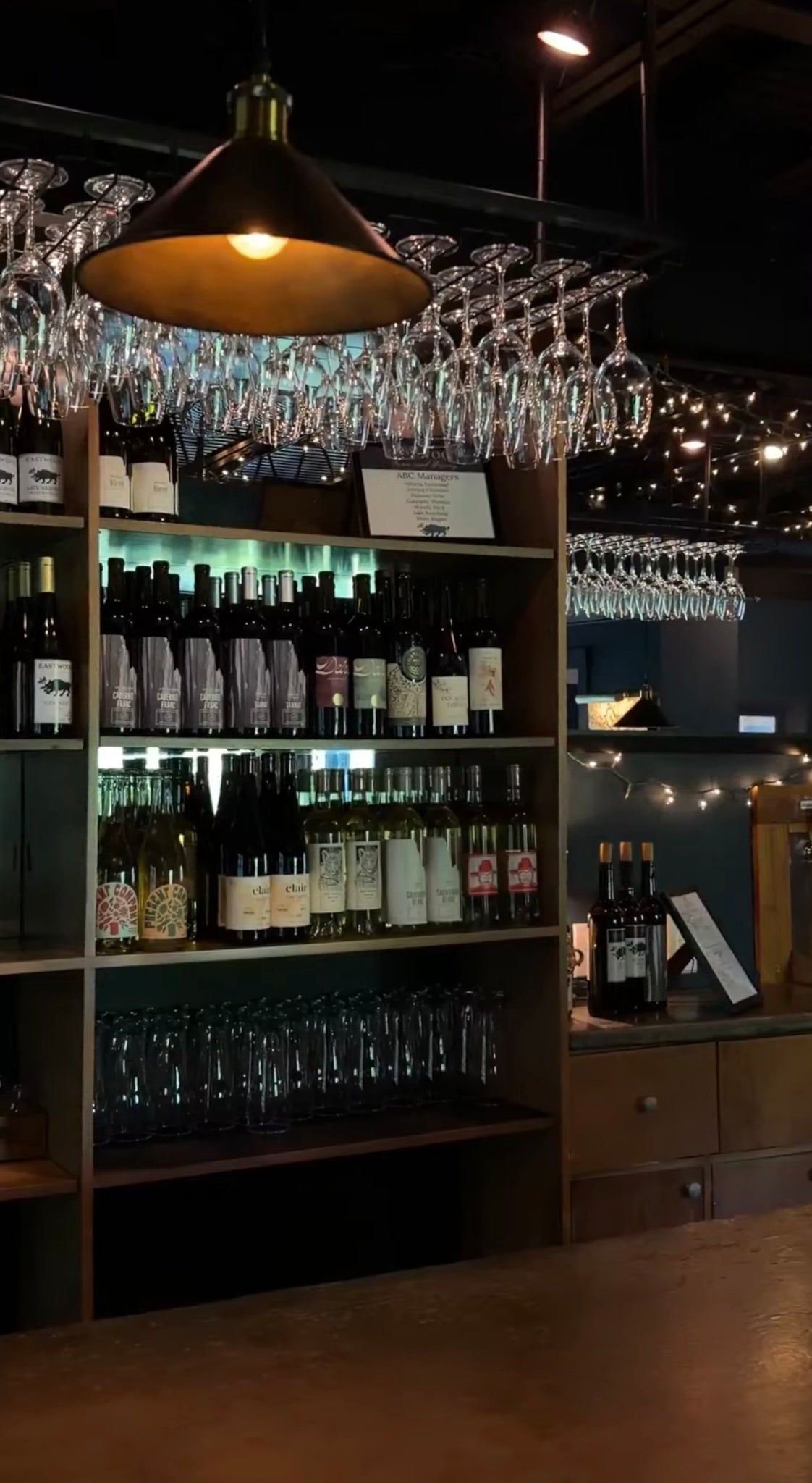 Wine bottles and glasses displayed in a bar setting with hanging lights.