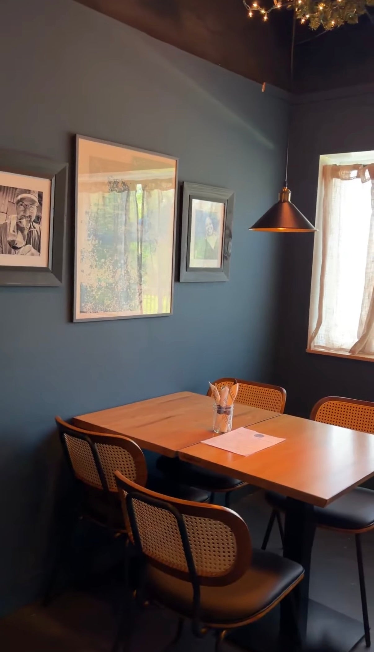 Dining area with a wooden table and chairs against a gray wall with framed pictures.