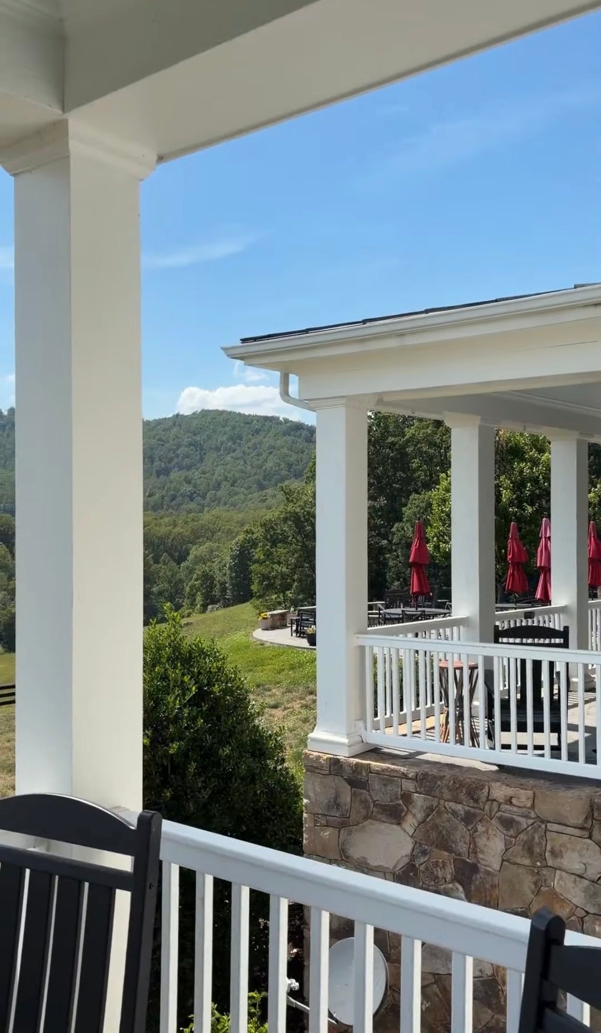 Porch with white railing and stone base, overlooking a scenic landscape with mountains and greenery.