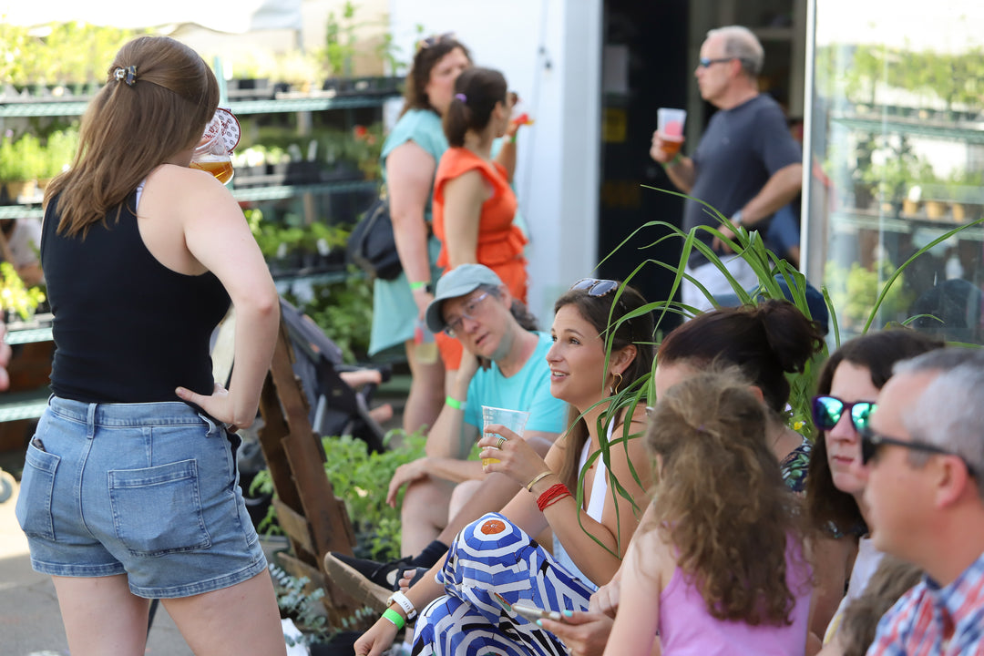 People sitting outdoors at a garden center, with plants and people in the background.