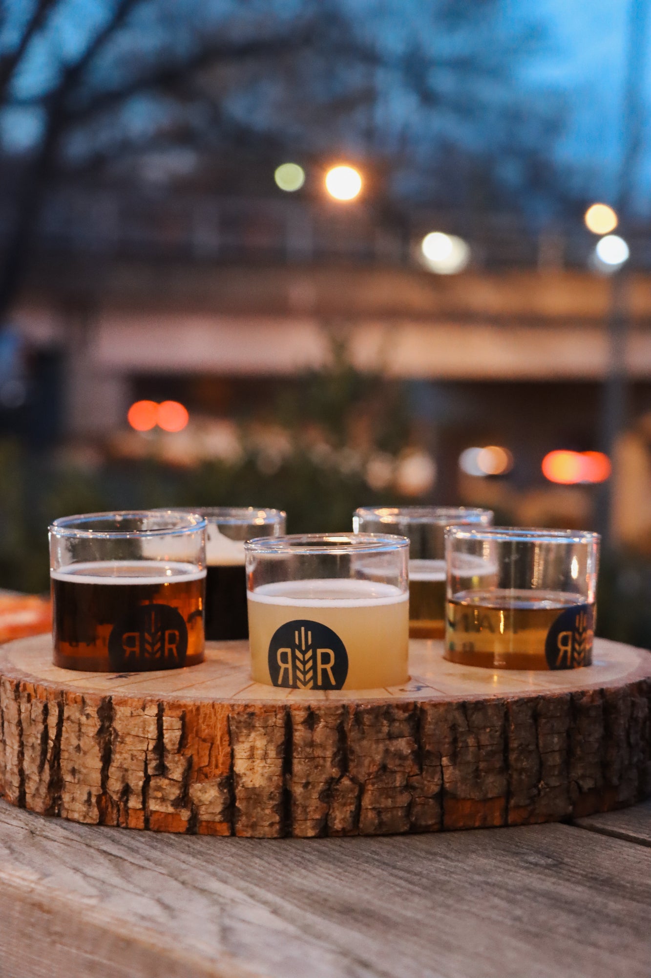 Five glasses of beer on a wooden tray with a blurred outdoor background