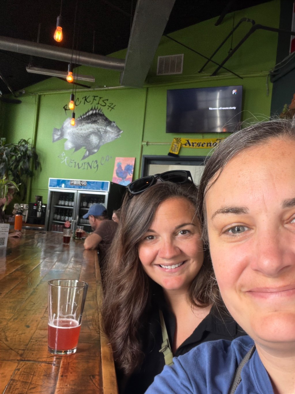 Two women sitting at a bar with a green wall and 'K&FISH' sign in the background.