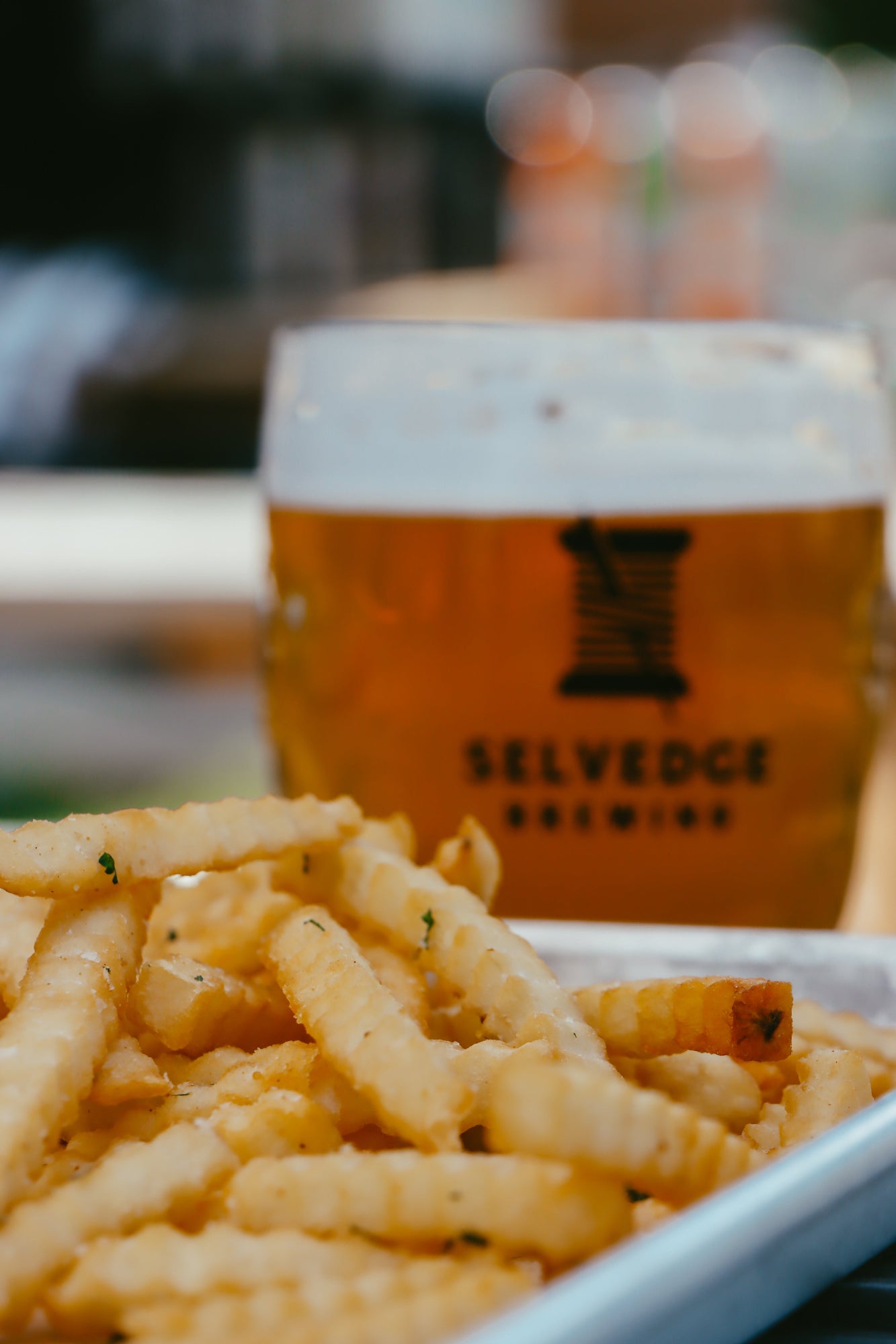 Fries in a container with a glass of beer from Selvedge Brewing in the background