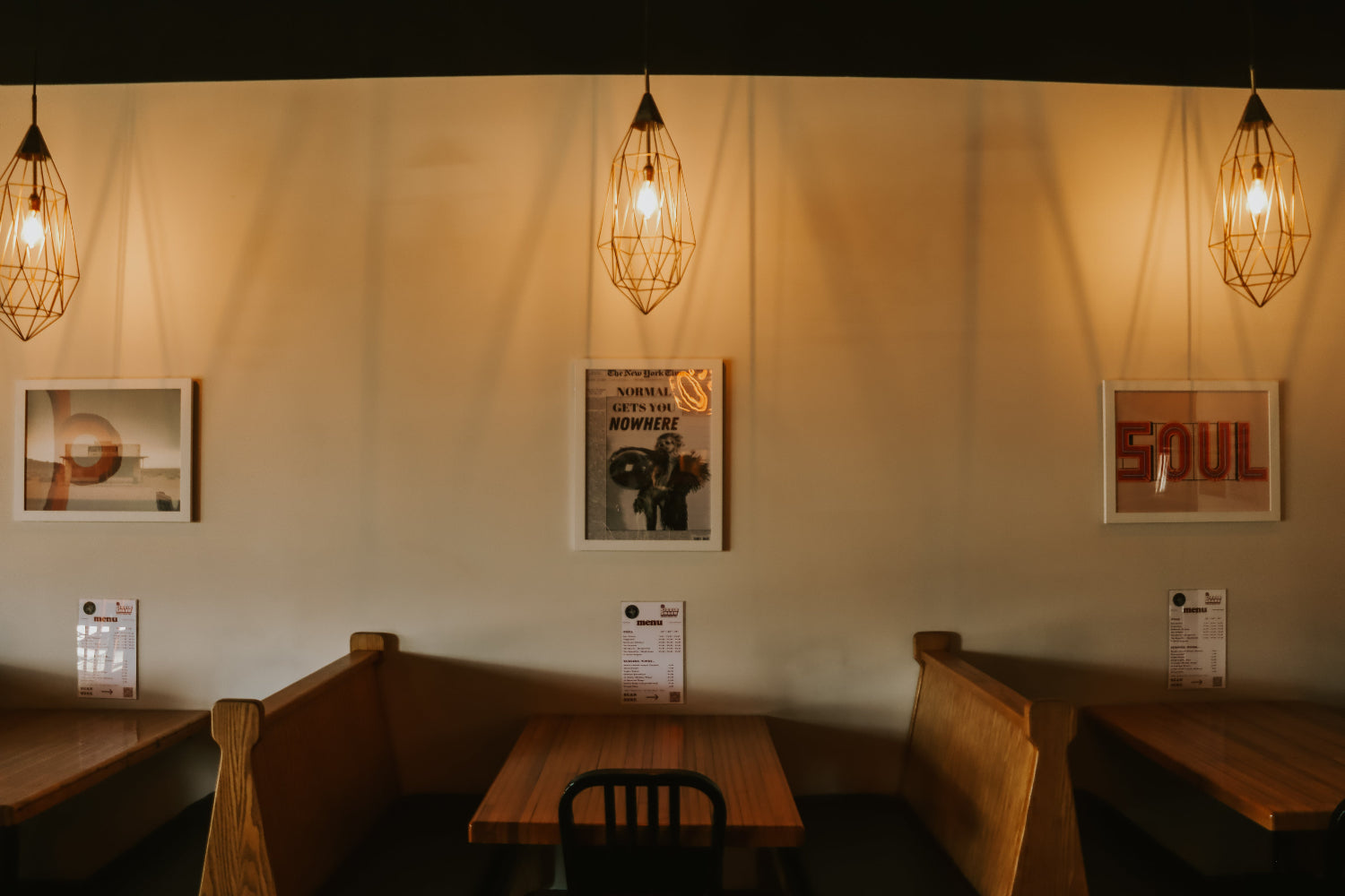 Dining area with wooden tables, chairs, and wall art in a warm setting.