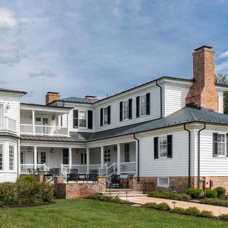 Large white house with a gray roof and brick chimney under a blue sky.